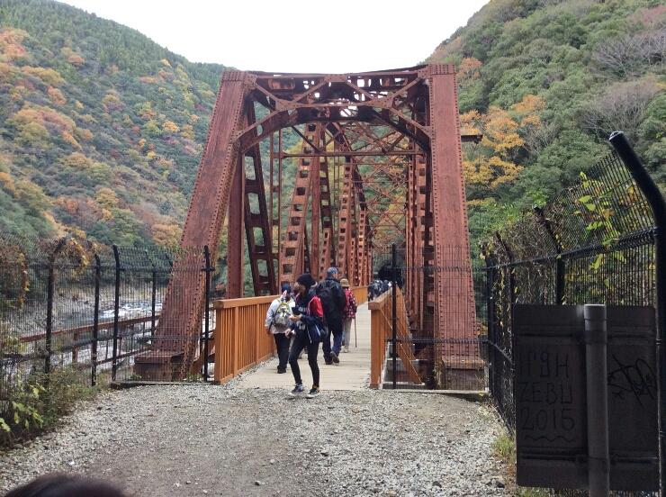 紅葉を背景にした鉄橋を渡る参加者の写真