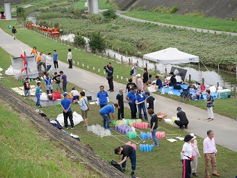 ペットボトルアートコンクール作品制作風景 河川敷でたくさんの人がペットボトルを並べている様子を堤防の上から撮った写真