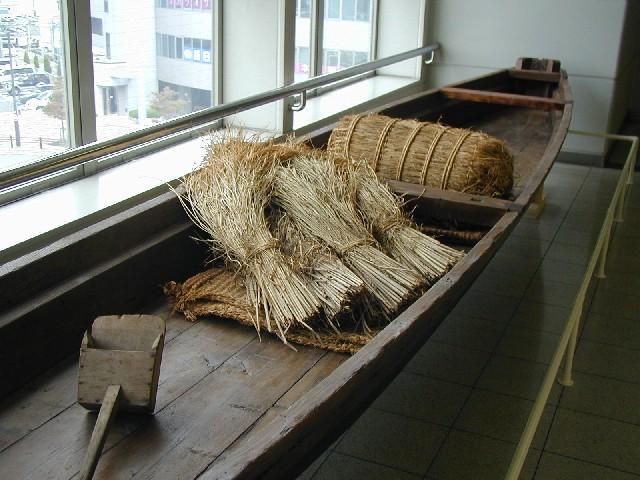 井路舟の乗るところに藁や藁の座布団、米俵や船を漕ぐための櫂がある写真